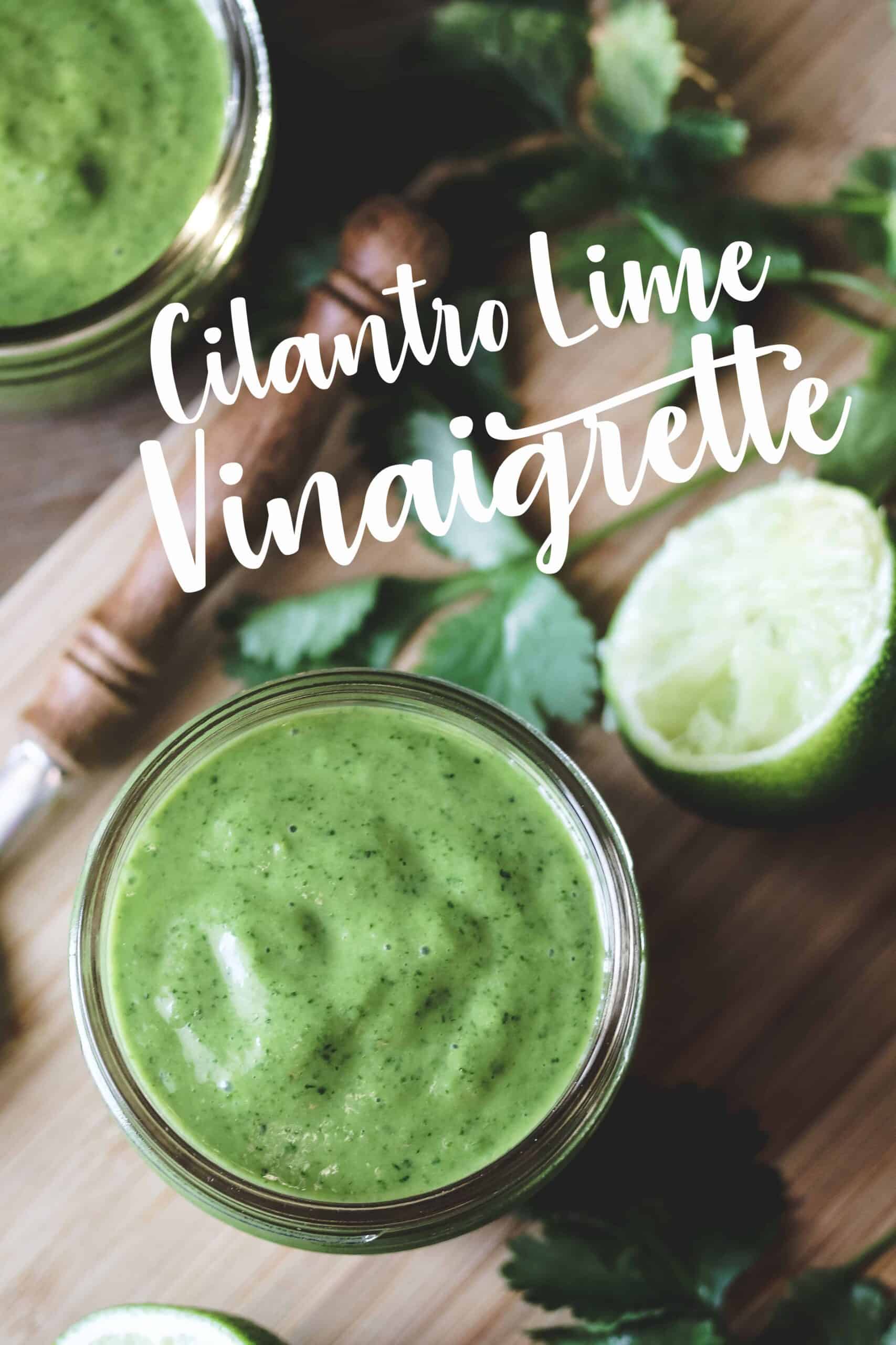 a jar of cilantro lime vinaigrette surrounded by limes and cilantro on a small bamboo cutting board.