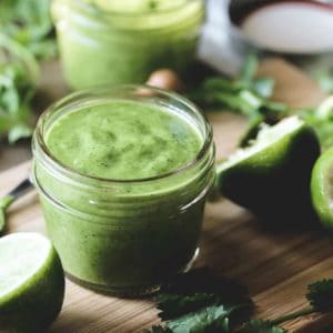 a jar of cilantro lime vinaigrette surrounded by limes and cilantro on a small bamboo cutting board.