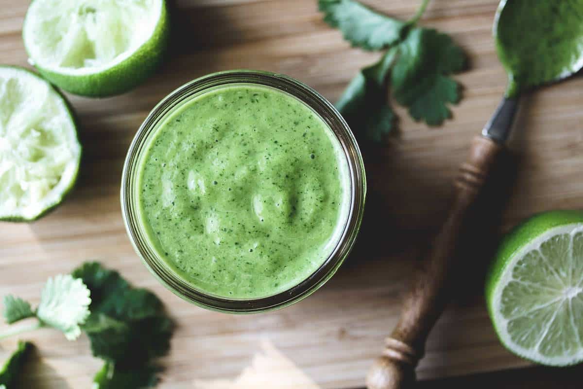 a jar of cilantro lime vinaigrette surrounded by limes and cilantro on a small bamboo cutting board.