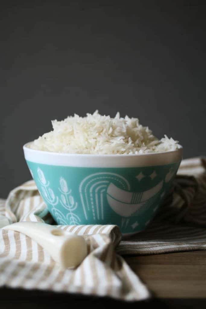 White rice in a white and teal pyrex bowl on a striped towel