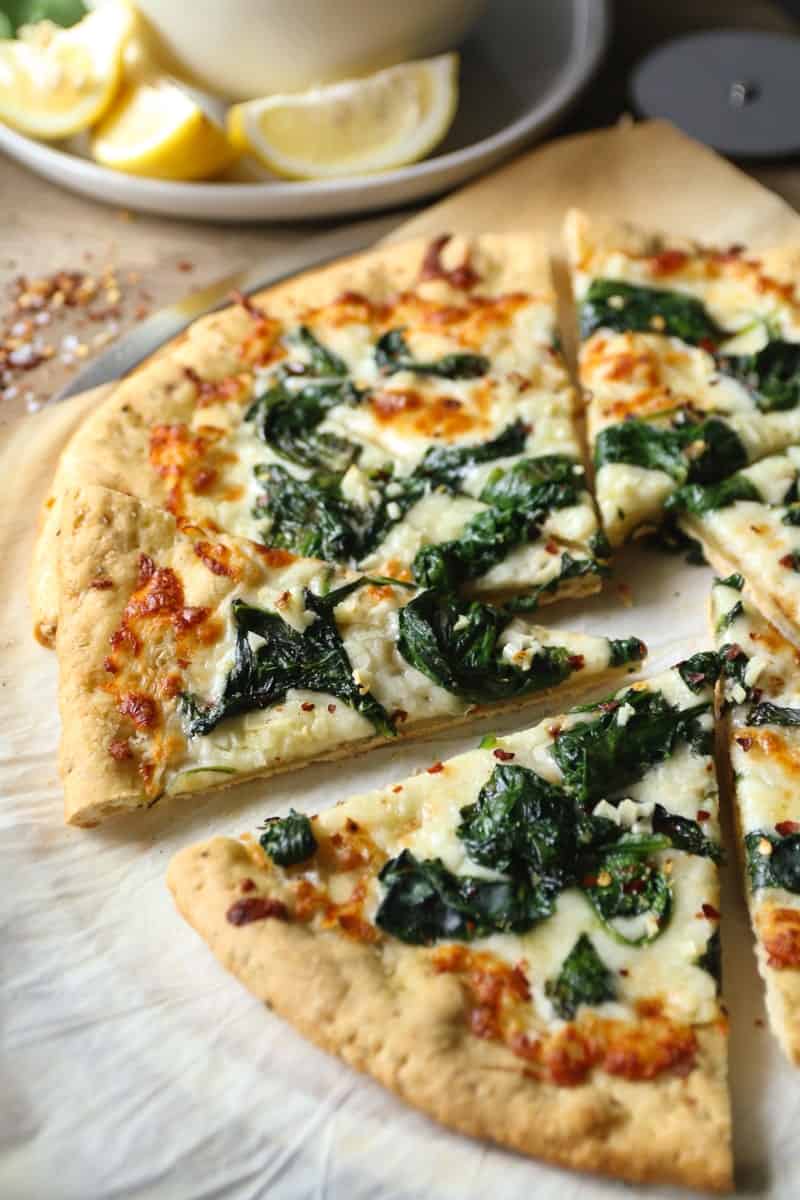 White pizza with spinach and garlic on parchment paper with lemon wedges