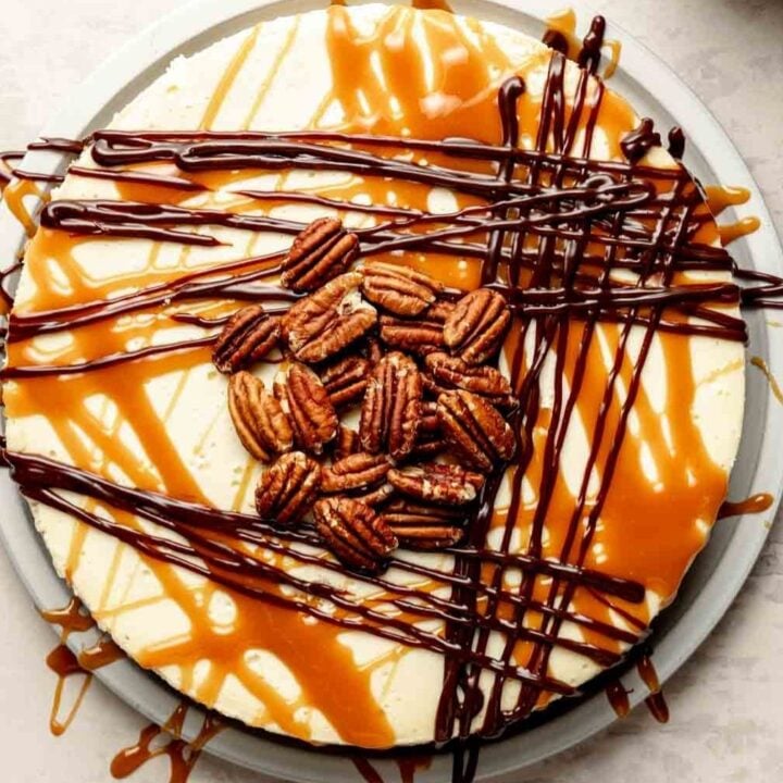 Turtle Cheesecake with chocolate fudge, caramel, and pecans on a cream plate, marble surface