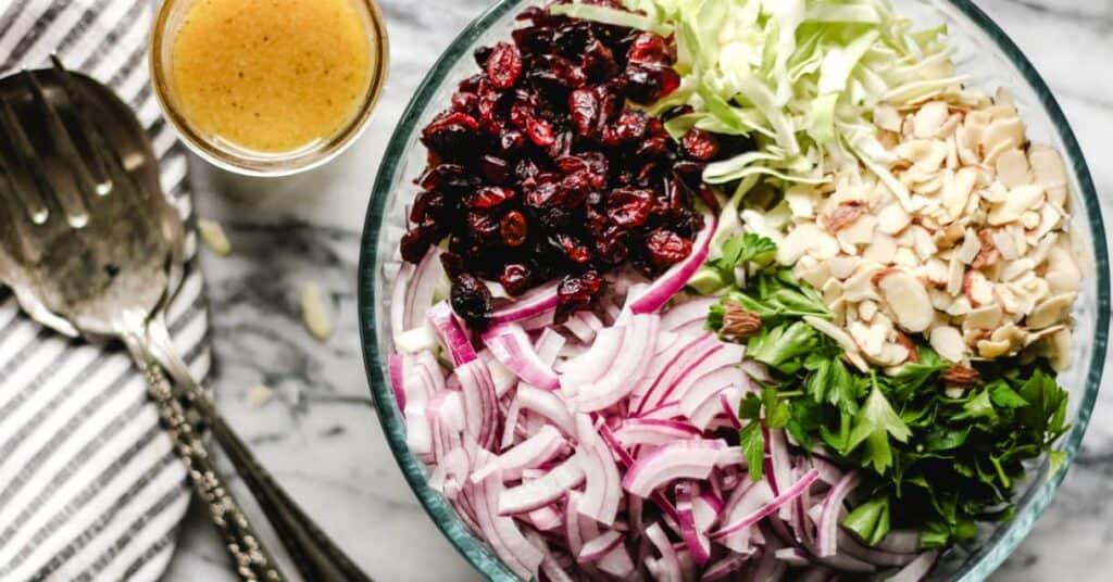 Cranberry Almond Thanksgiving Slaw in a large bowl, ingredients separated, apple cider vinaigrette on the side.