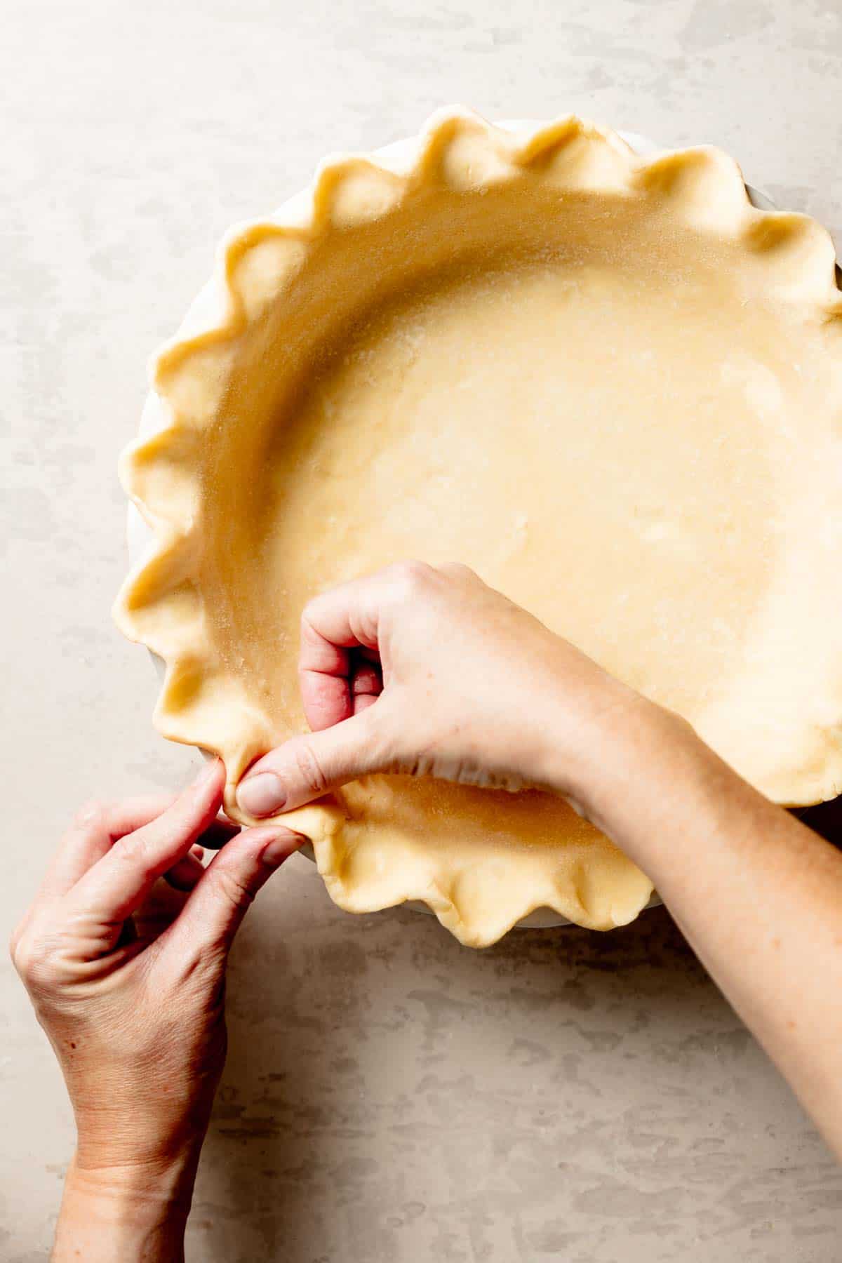 Hands crimping gluten-free pie crust in pie dish.