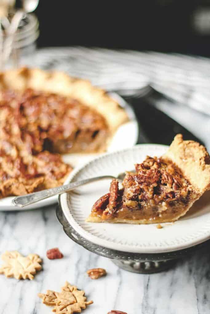 a slice of pumpkin pecan pie on a dessert plate, small pie crust leaves on a marble surface, pie in the background
