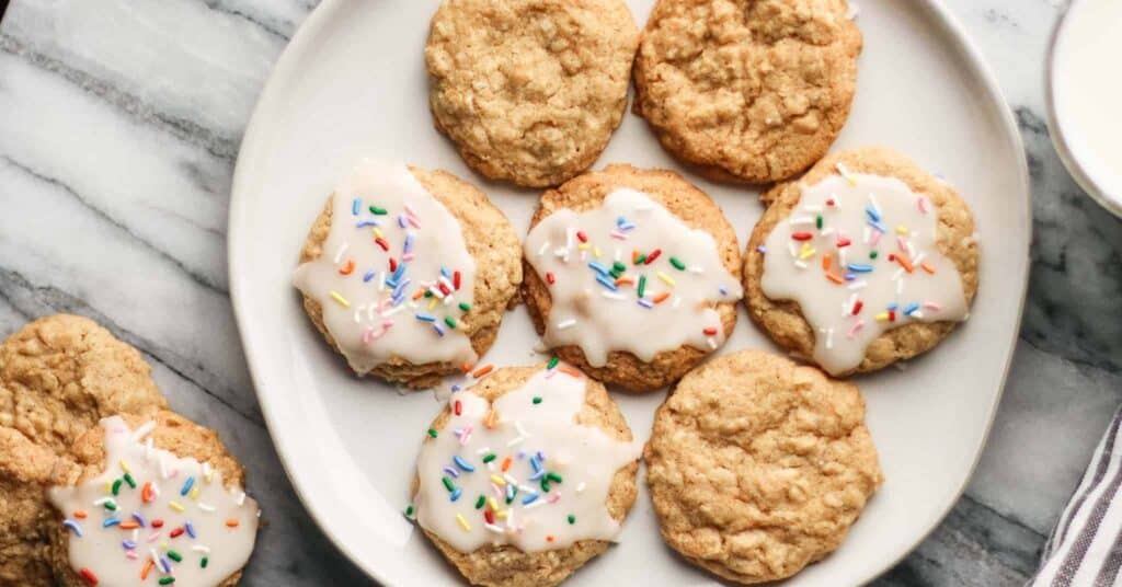 a plate of oatmeal cookies, some have icing and rainbow sprinkles