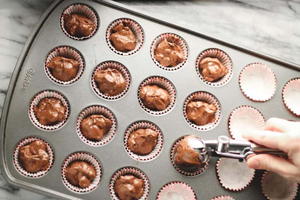 mini muffin tin with liners being filled with crockpot candy