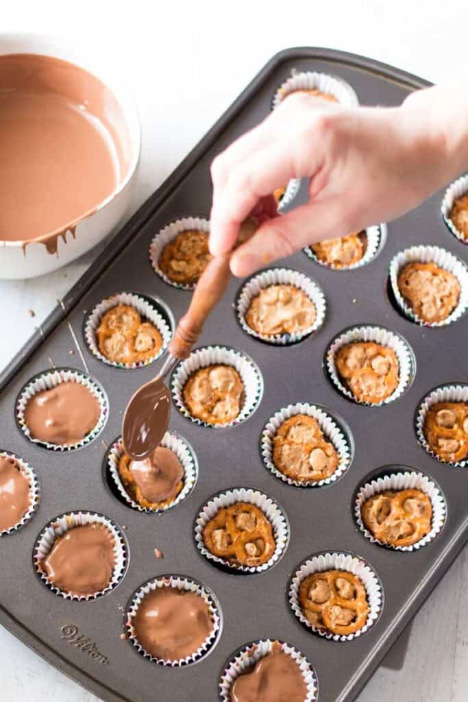 pouring melted milk chocolate over the pretzel, peanut butter, rolo combination in the muffin tin