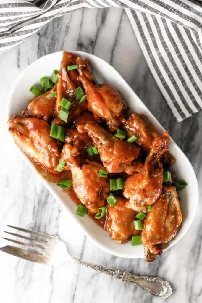 Honey Sriracha BBQ Wings on a white oval dish sprinkled with green onions