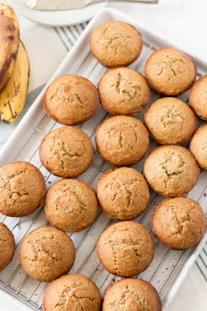 A dozen gluten free banana muffins on a wire rack, on a speckled baking sheet.