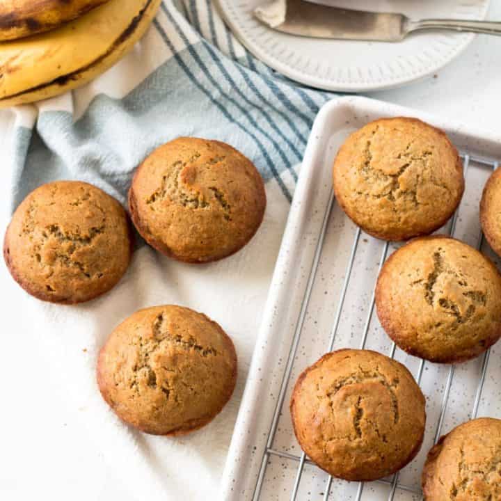 Gluten free banana muffins, one with butter, ripe bananas in background