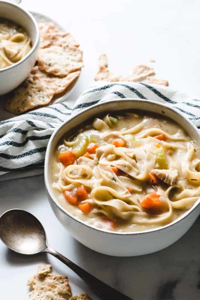 a bowl of chicken noodle soup with crackers on the side.