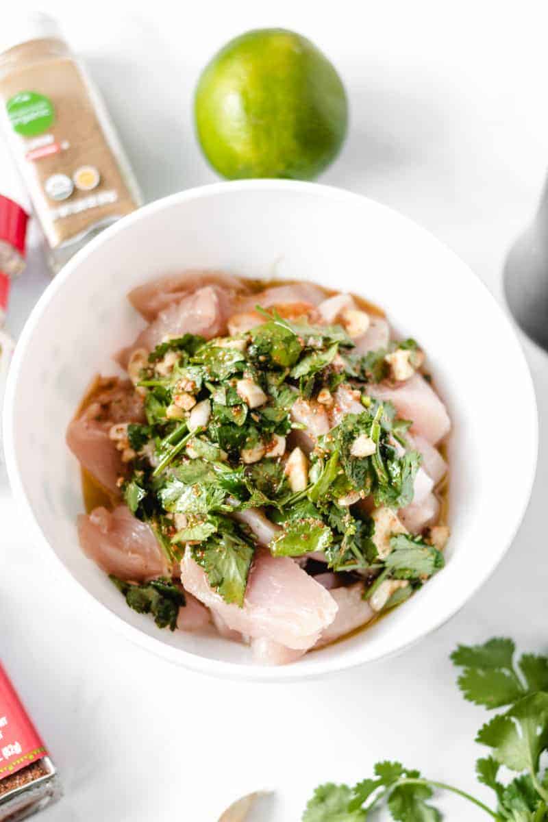 Fajita marinade with lots of cilantro over chicken strips in a white bowl.