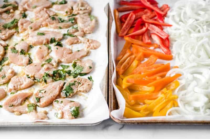 Chicken fajitas on two sheet pans, one with chicken, the other with bell peppers and onion.