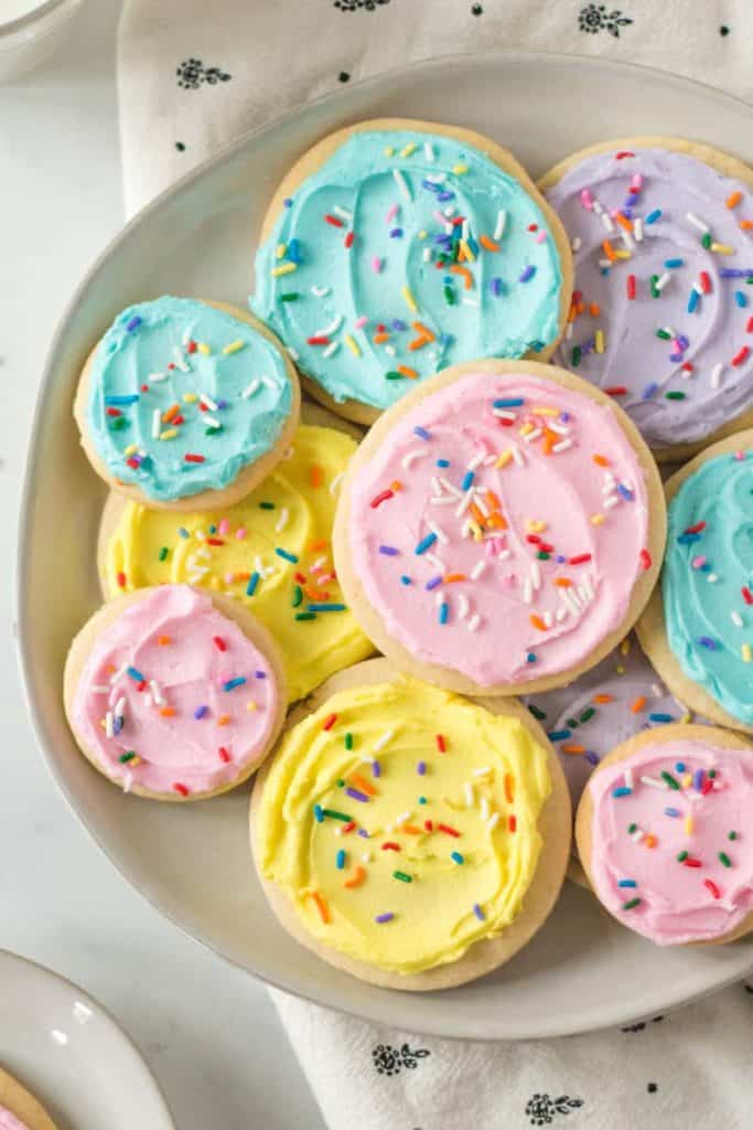 Plate full of pastel frosted gluten-free sugar cookies with rainbow sprinkles.