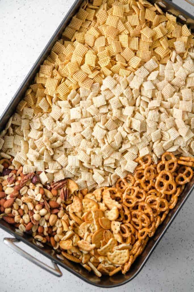 A large roasting pan filled with rice chex, corn chex, gluten-free pretzels, crackers, and mixed nuts.