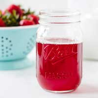 Bright red strawberry simple syrup in a glass mason jar.