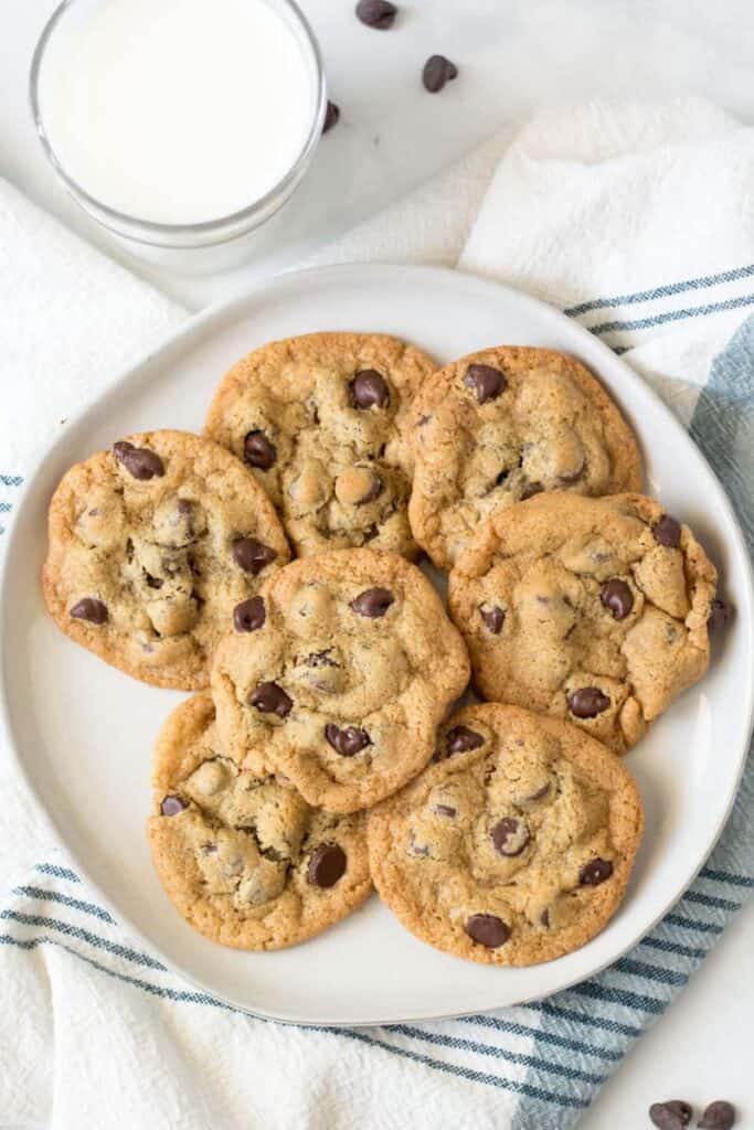 A plate full of chocolate chip cookies next to a glass of milk.