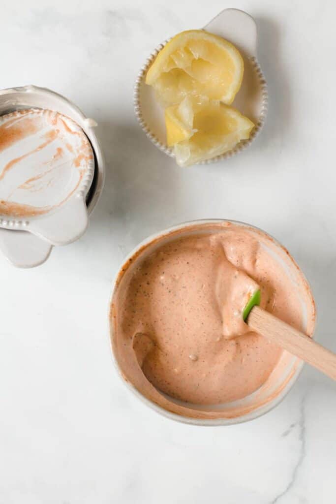 Chipotle mayo stirred together, empty dishes next to it and a spent lemon wedge.