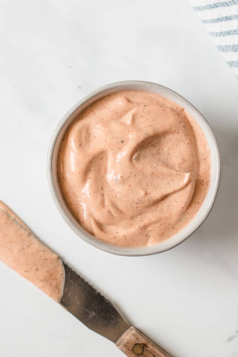 Chipotle Mayo in a small bowl with spreader knife and striped towel beside it. 