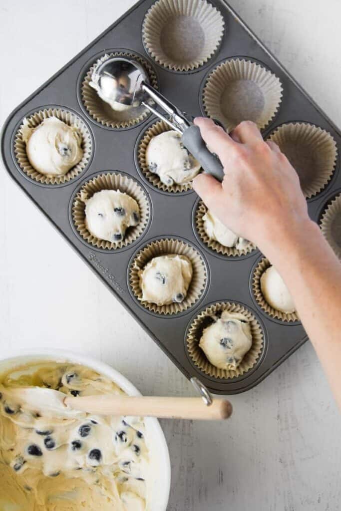 Scooping muffins into parchment cupcake liners in muffin tin.