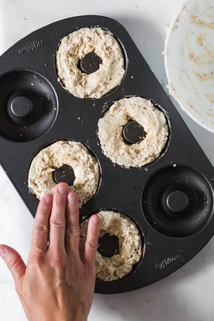 Bagel mixture spooned into a donut pan, patted down with wet fingers.