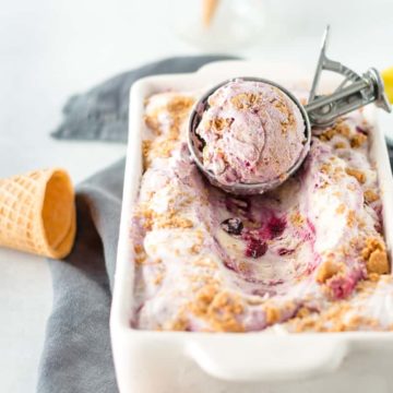 Blueberry Cheesecake ice cream in a loaf pan with ice cream in a scoop resting on top.