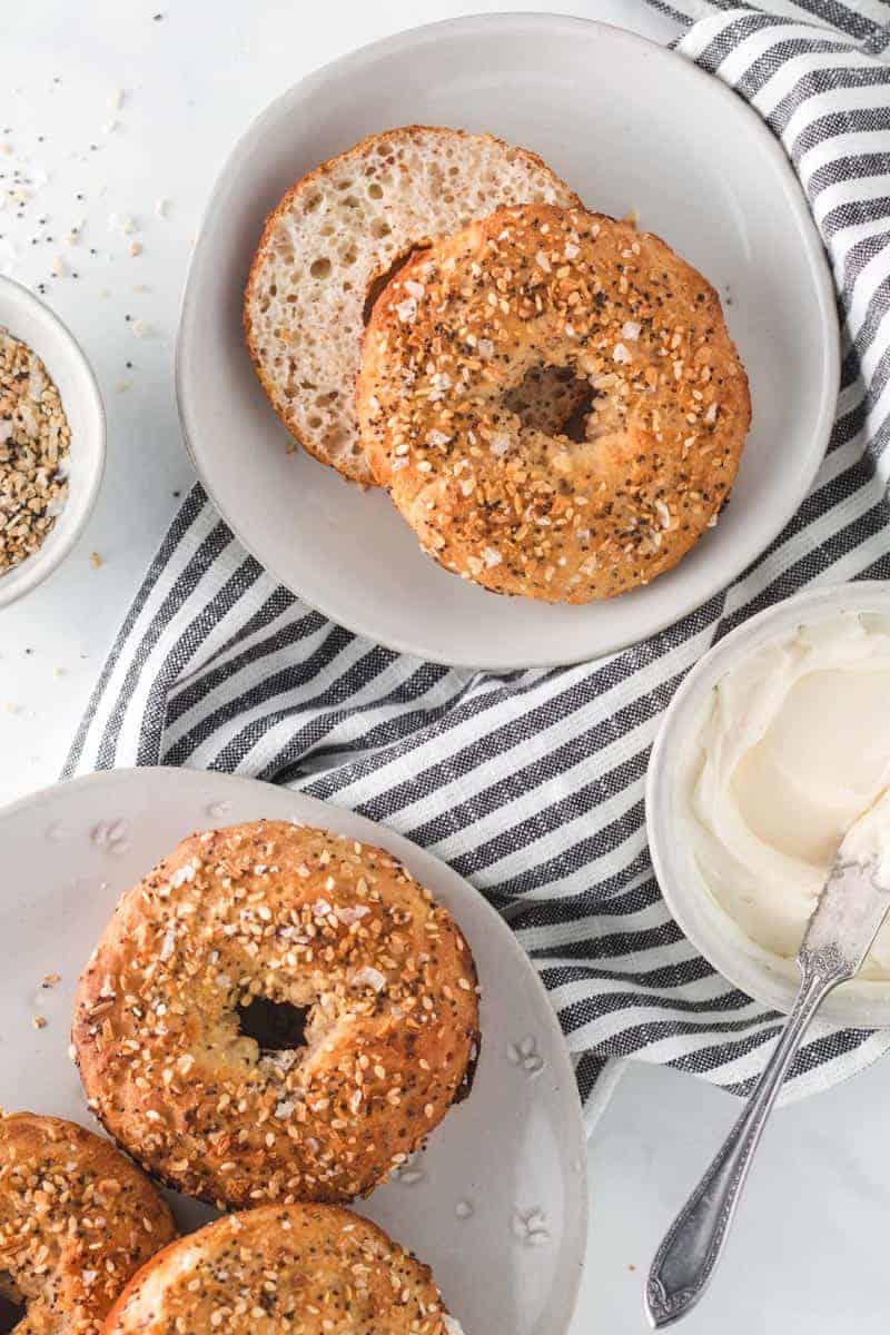 two ingredient bagels on a table with cream cheese, one cut in half.