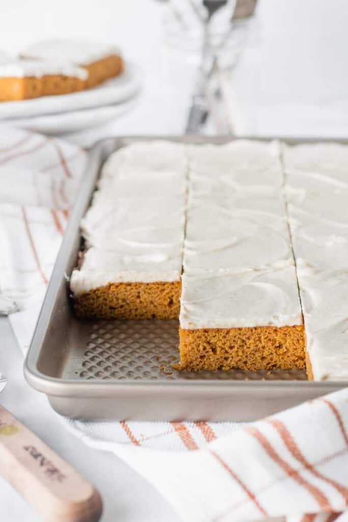 A sheet pan with sliced frosted pumpkin bars. Several missing to show texture of cake.