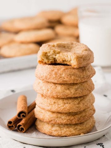 A stack of snickerdoodle cookies, gluten-free, next to cinnamon sticks and a glass of milk.