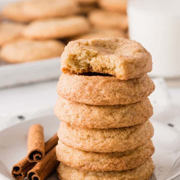 A stack of snickerdoodle cookies, gluten-free, next to cinnamon sticks and a glass of milk.
