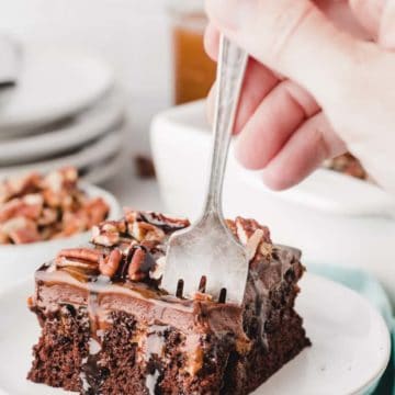 Chocolate turtle poke cake slice on plate dripping with chocolate sauce.