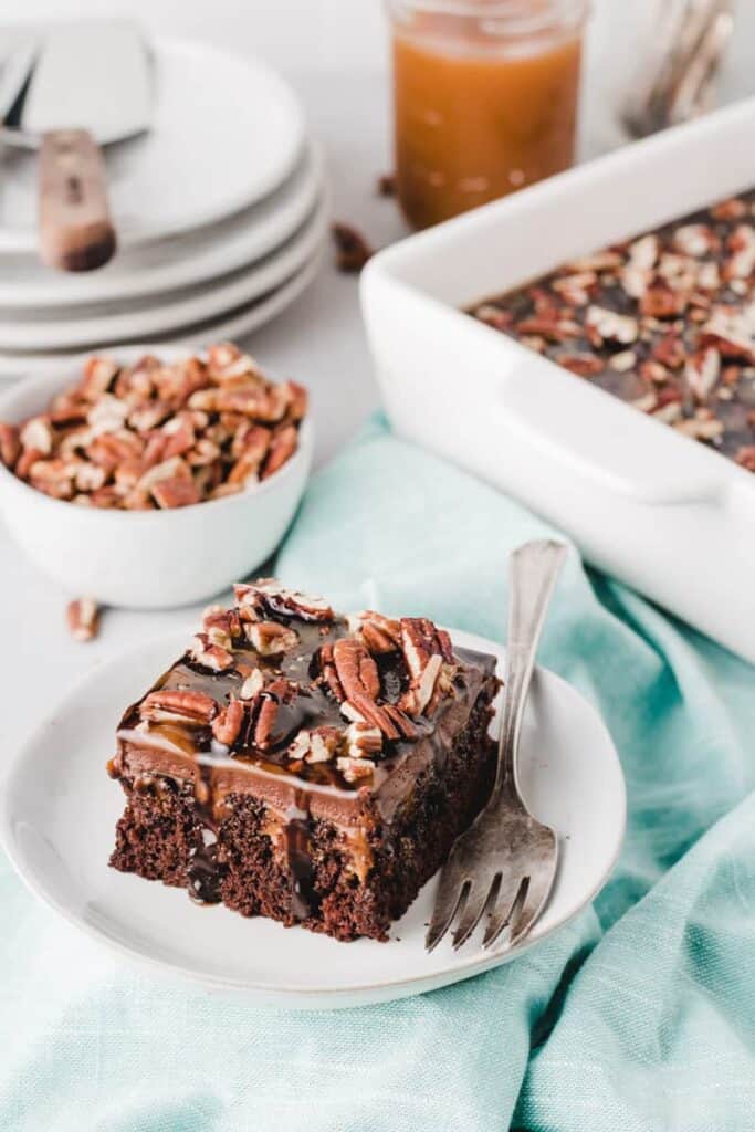 Chocolate turtle poke cake slice on plate dripping with chocolate sauce.