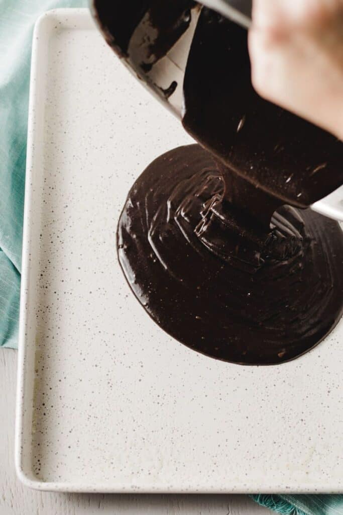 Pouring dark chocolate cake batter into greased speckled sheet pan.