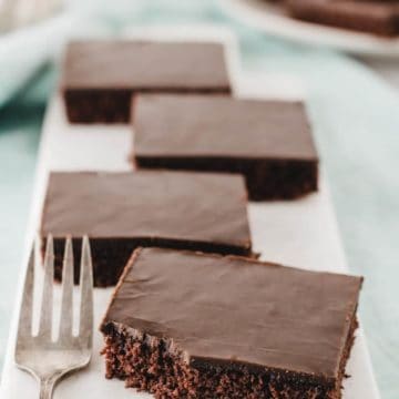 Four slices of gluten-free Texas sheet cake on a marble slab, one with a bite taken from the corner.