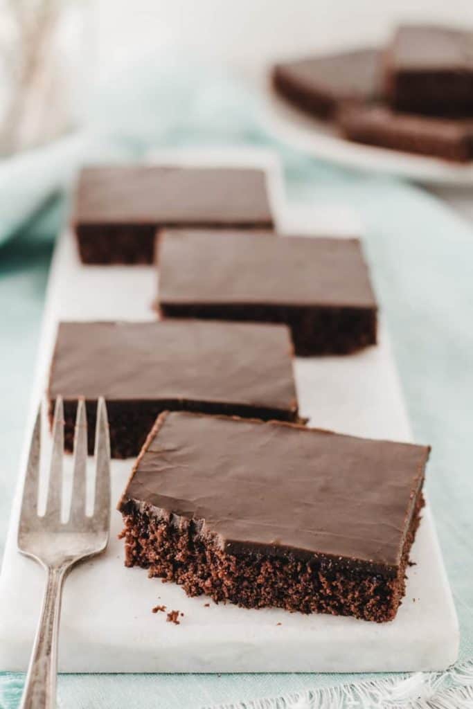 Four slices of gluten-free Texas sheet cake on a marble slab, one with a bite taken from the corner.