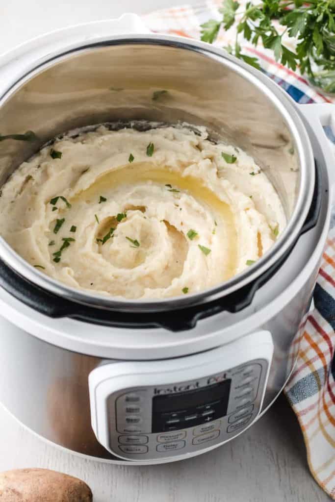 A white instant pot full of mashed potatoes with butter and parsley on top.