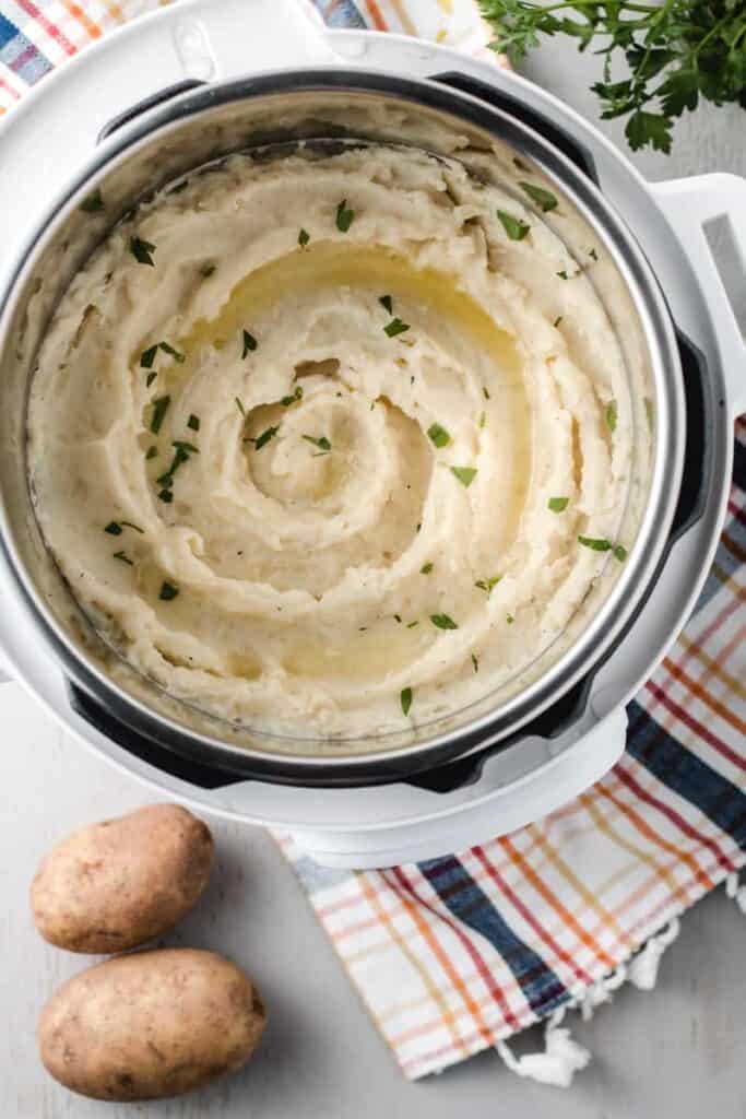 Mashed potatoes swirled in a white instant pot with melted butter and parsley sprinkled on top.