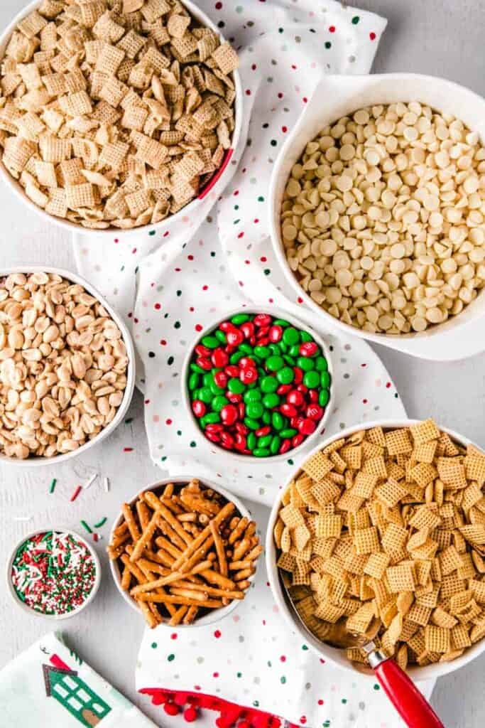 Ingredients for Christmas Chex mix portioned out in bowls, including red and green m&m's and festive sprinkles.