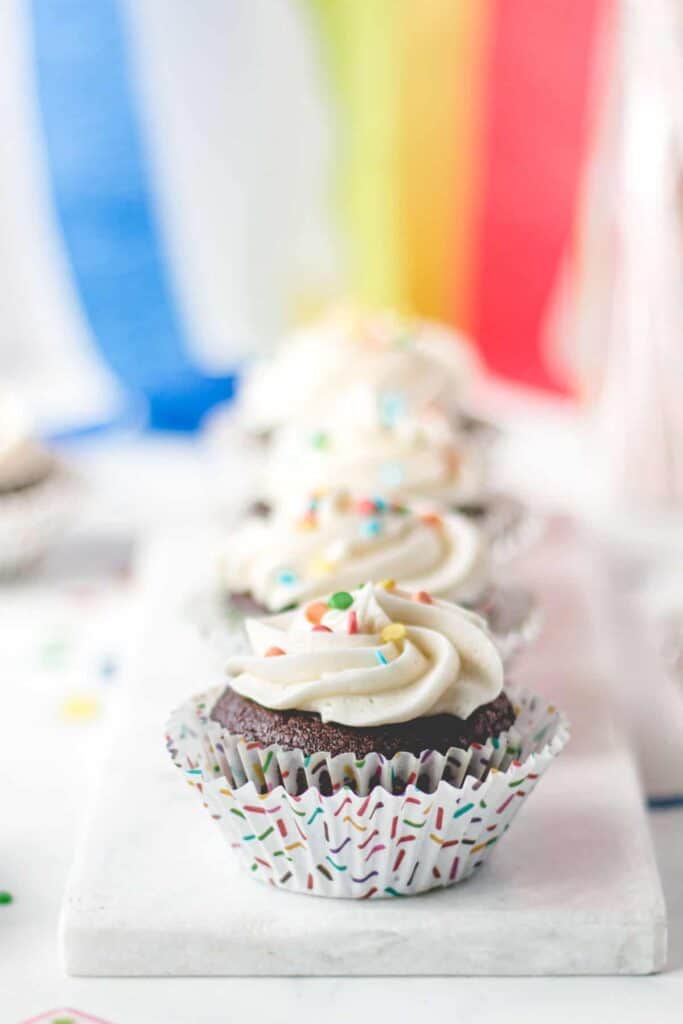 Gluten-free chocolate cupcakes with vanilla frosting and rainbow sprinkles in rainbow sprinkle cupcake wrappers.