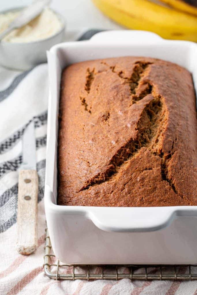 A loaf of perfectly baked, gluten-free banana bread in the pan with a domed and cracked top.