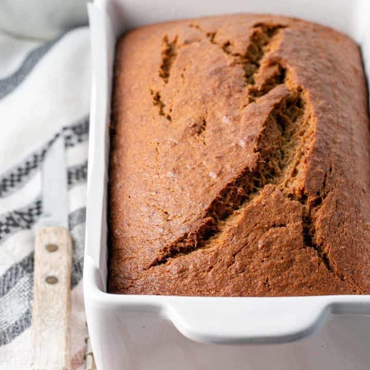 A loaf of gluten-free banana bread in loaf pan with a perfectly domed and cracked top.