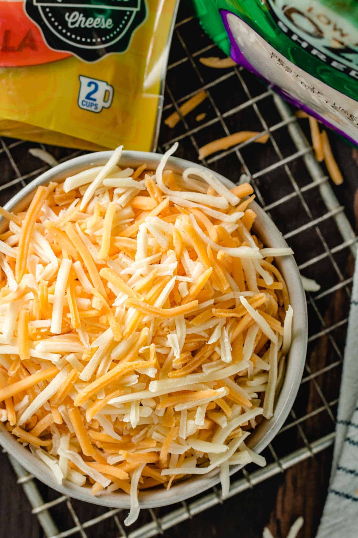 A bowl of pre-shredded cheddar-jack cheese on a brown table.