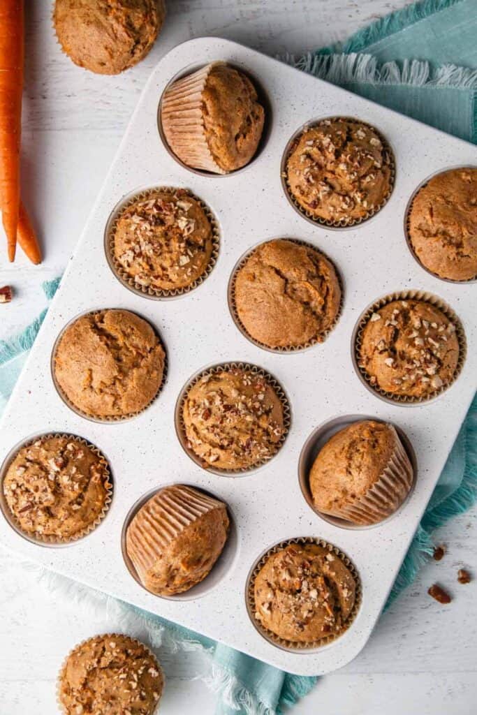 The baked gf carrot muffins in a white speckled tin. Some muffins tilted on side.