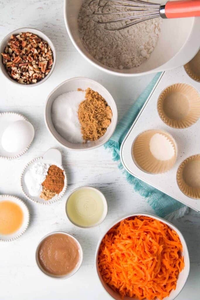 Ingredients for gluten-free carrot muffins measured in bowls.  A whisk rests in the bowl of flour.