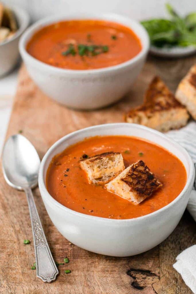 Gluten-free tomato soup in bowls next to a nicely toasted grilled cheese sandwich.