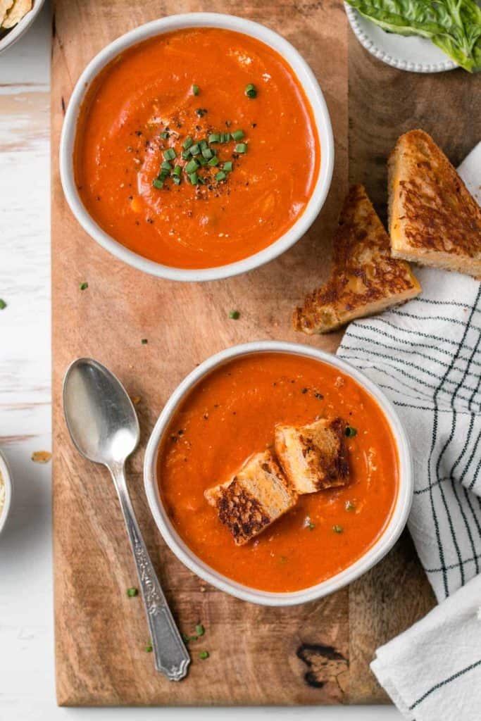 Homemade gluten-free tomato soup in bowls, topped with chives and grilled cheese croutons.