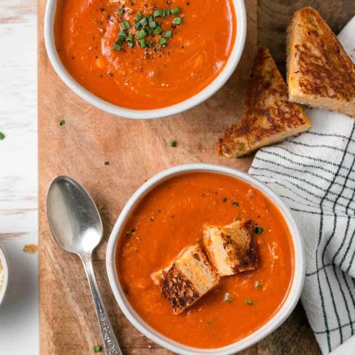 Gluten-free tomato soup in bowls with chives and grilled cheese.