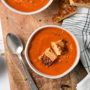 A bowl of creamy homemade gluten-free tomato soup with grilled cheese croutons on top.