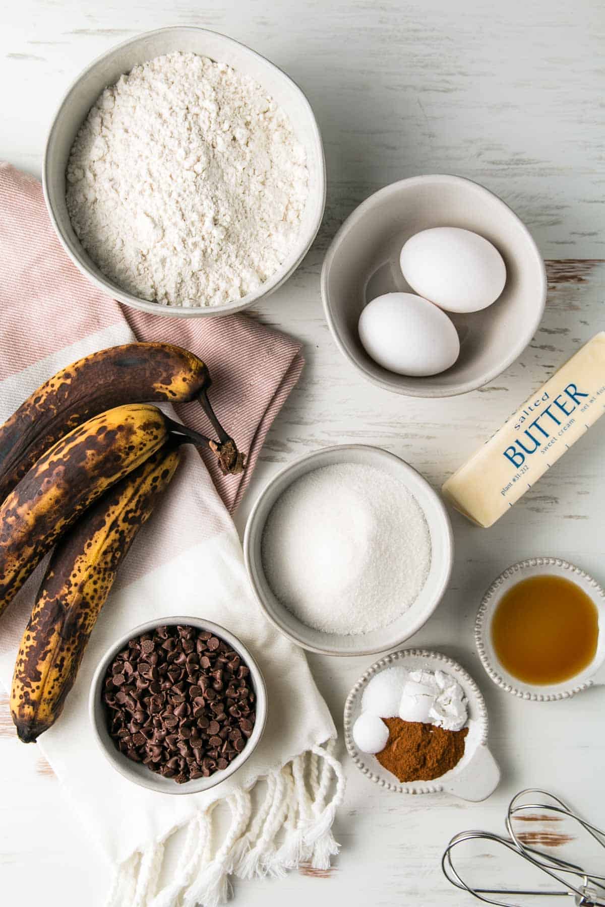 Ingredients for gluten-free chocolate chip banana muffins measured out in bowls next to three over-ripe bananas.